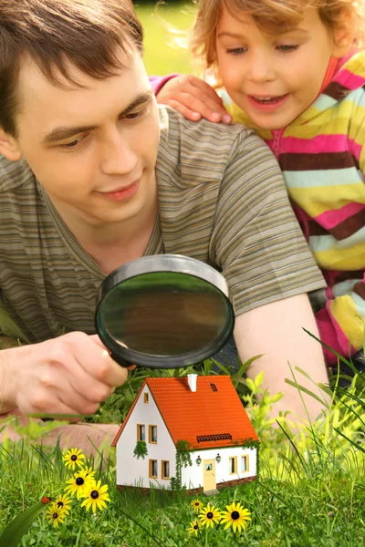 Отец с маленькой девочкой смотрит на маленький дом через лупу — стоковое фото