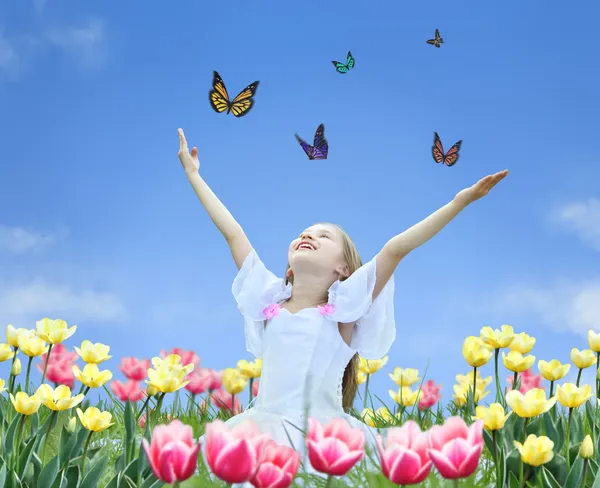 Little girl in tulips with hands up and butterfly collage — Stock Photo, Image