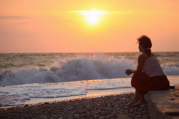 Silhueta sentado jovem mulher no pôr do sol praia ondulada — Fotografia de Stock