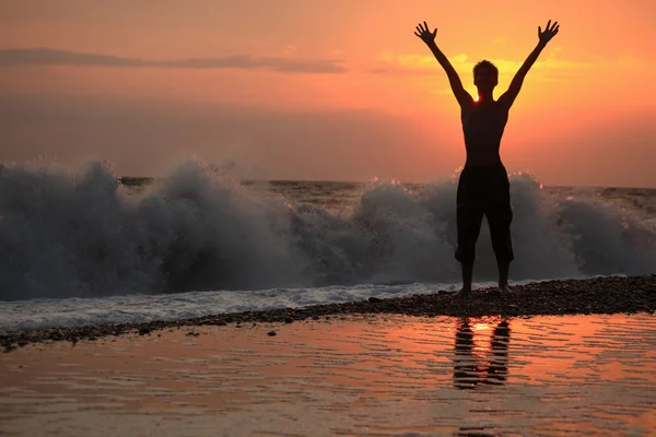 Silueta chico levantó las manos hacia arriba en la puesta del sol playa ondulada — Foto de Stock