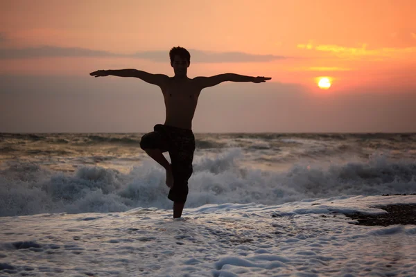 Silueta chlap jógu na pláži při západu slunce vlnité — Stock fotografie