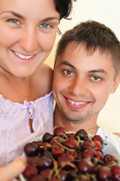 Улыбающийся мужчина и молодая женщина едят вишни — стоковое фото