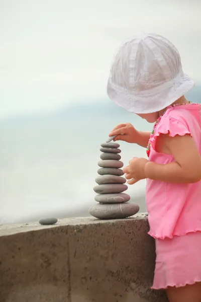 Girl hat is building a construction from pebble stones — Stock Photo, Image