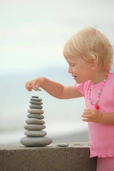 Chapéu menina está construindo uma construção de pedras de seixos — Fotografia de Stock