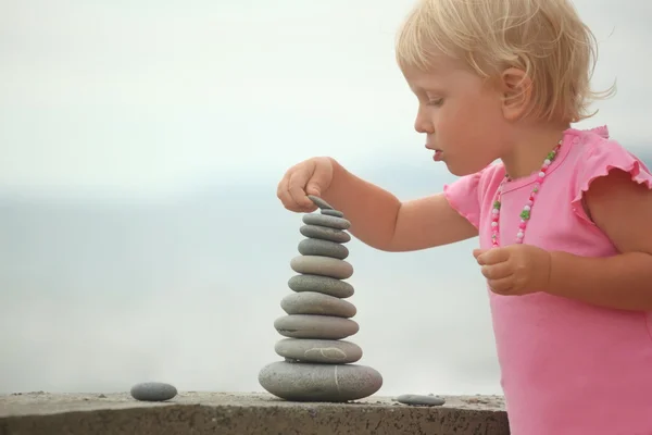 Chapéu menina está construindo uma construção de pedras de seixos — Fotografia de Stock