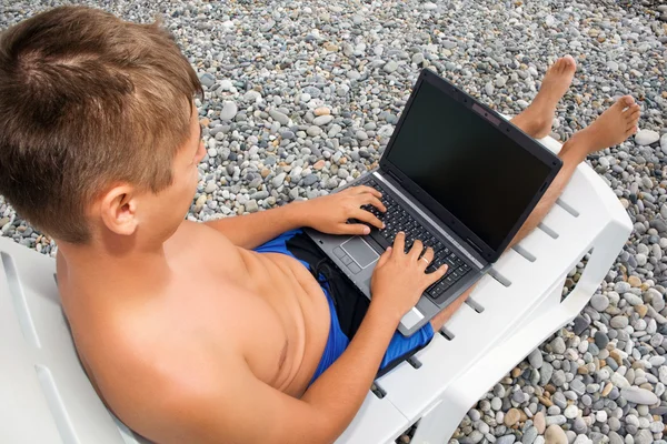 年轻男子斜倚在贵妃椅上多石的海滩，看着 — 图库照片