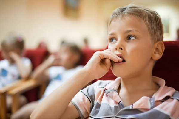 Niño sentado en sillón de cine, sosteniendo los dedos cerca de la boca — Foto de Stock