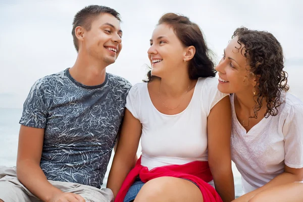 Smiling man and two young beautiful women sitting on beach, Loo — Stock Photo, Image