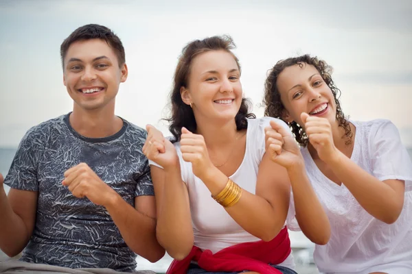 Smiling man and two young women dancing sitting on beach — Stock Photo, Image