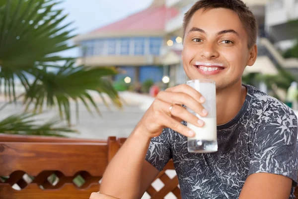 Junger lächelnder Mann sitzt in einer Laube auf dem Ferienort und trinkt Kefir — Stockfoto