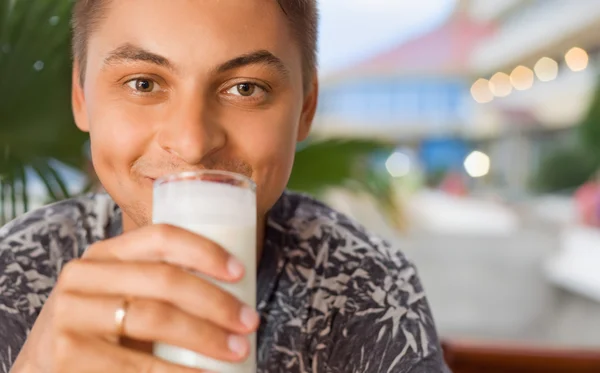 Молодой улыбающийся человек пьет кефир сидя в беседке на курорте — стоковое фото
