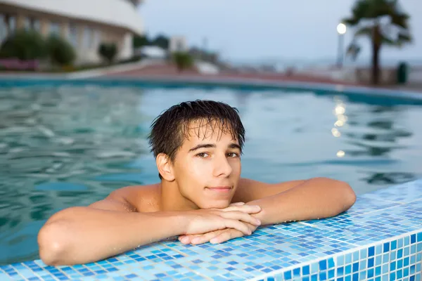 Adolescente menino relaxante perto borda na piscina ao ar livre, olhando para ca — Fotografia de Stock