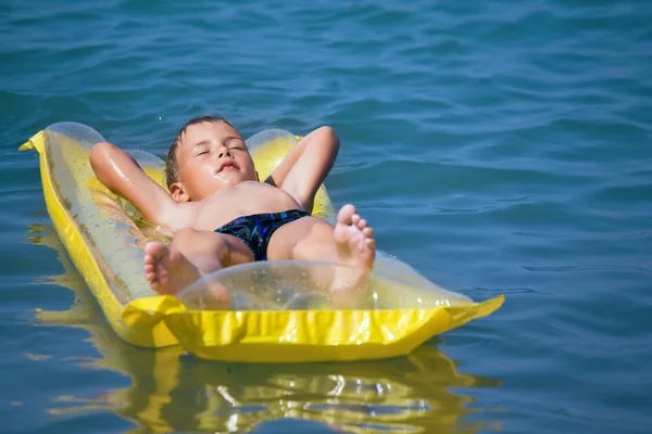 Niño en traje de baño azul oscuro relajándose en un mate inflable —  Fotos de Stock