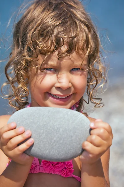 Smiling pretty little girl holds in hands pebble on seacoast in — Stock Photo, Image
