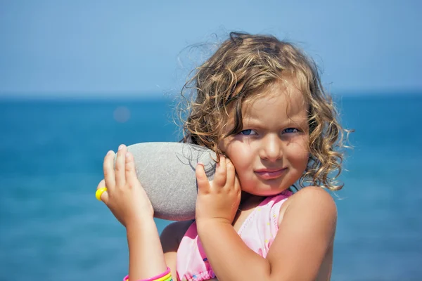 Pretty little girl holds in hands pebble on seacoast in afternoo — Stock Photo, Image