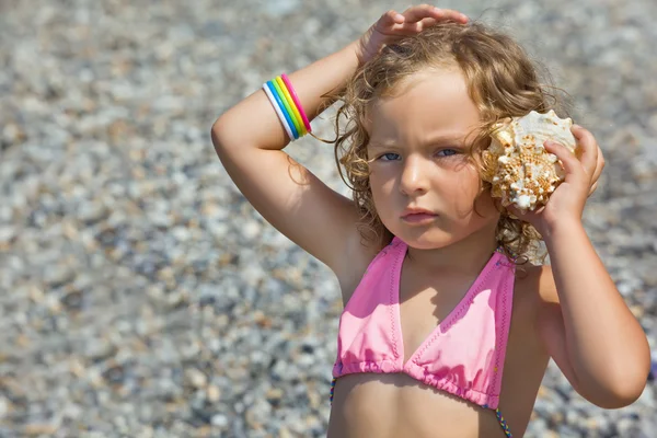 Sevimli küçük kız seashell kase sahil üzerinde bir kulak için eğildim — Stok fotoğraf