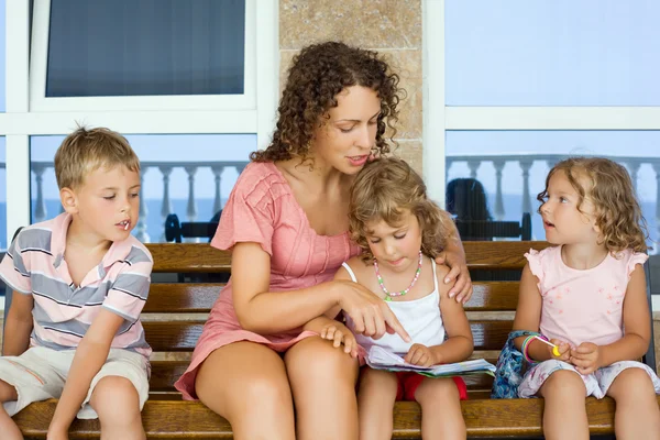 Young beautiful woman reads book to two little girls and boy on — Stock Photo, Image