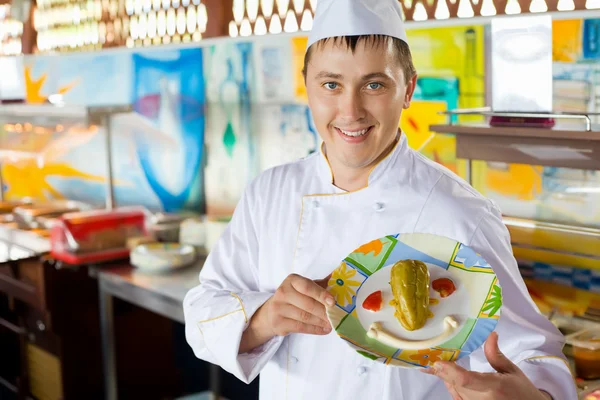 Cozinheiro alegre em uniforme que segura em prato de mãos com salada em para — Fotografia de Stock