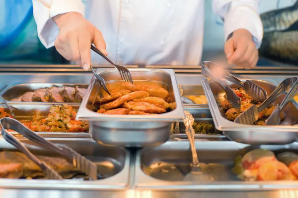 La mano del cocinero toma las pinzas de carne frita en el mostrador de almuerzo en público —  Fotos de Stock