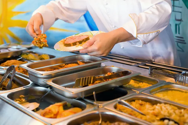 Manos de cocinero poniendo en plato ragú vegetal en cateri público —  Fotos de Stock