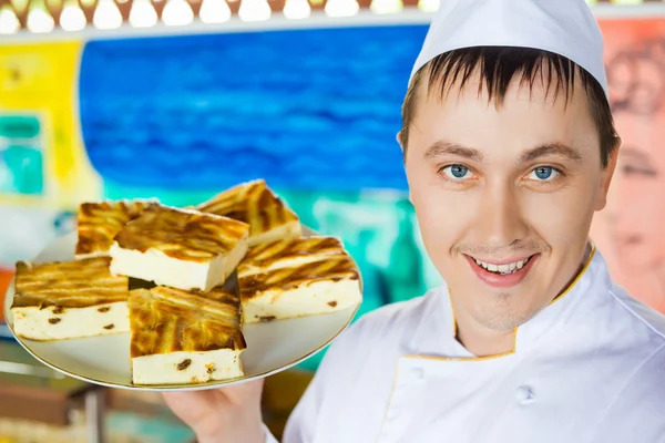 Веселый повар в униформе держит сыр запеченный пудинг на блюде — стоковое фото