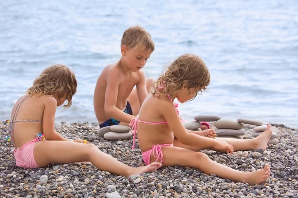 Niños tres juntos sentados en la playa de piedra, crea pirámide —  Fotos de Stock