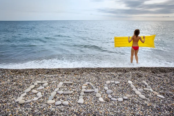 Inscripción de piedras PLAYA en la costa pedregosa, mujer joven mantiene —  Fotos de Stock