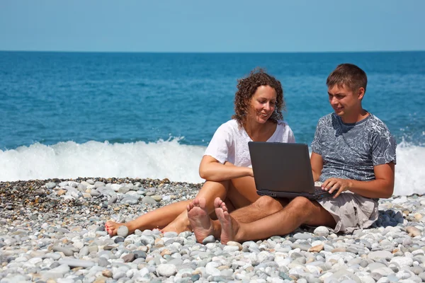 Man and girl on seashore with laptop — Stock Photo, Image