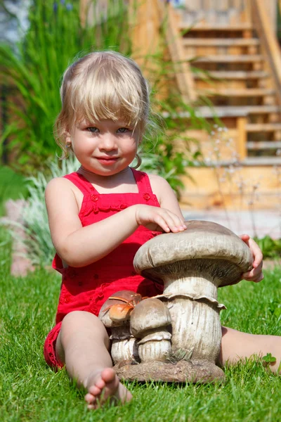 A menina em um gramado senta-se com um cogumelo de brinquedo — Fotografia de Stock
