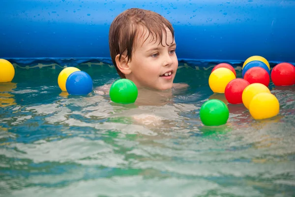 O menino flutua na piscina inflável com bolas multicoloridas . — Fotografia de Stock