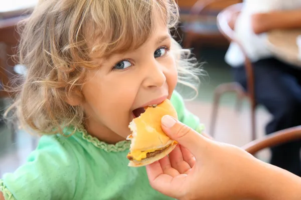 Pretty little girl eats hamburger from mothers's hand — Stock Photo, Image