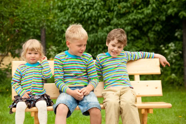 Troje dzieci na ławce w identyczne ubrania — Zdjęcie stockowe