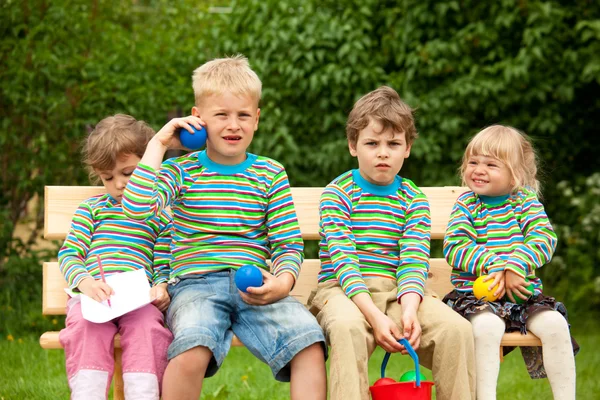Two boys and two girls on a bench in park. In identical stripe c — Stock Photo, Image