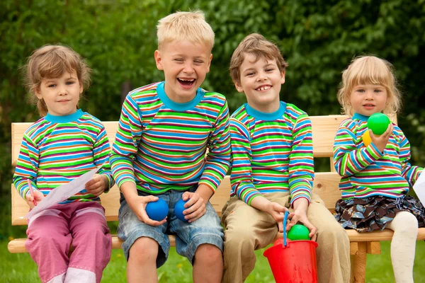 Τέσσερα παιδιά στην ίδια ρούχα γέλιο συνεδρίαση σε έναν πάγκο. — Φωτογραφία Αρχείου