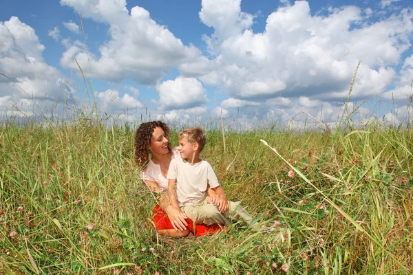Mujer joven y niño sonriente sentado en el prado, Mirando contra e —  Fotos de Stock