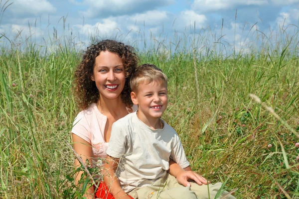 年轻女子和微笑的男孩坐在草地上 — 图库照片