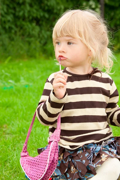 The little girl paints lips in park — Stock Photo, Image