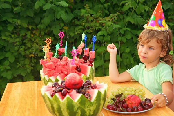 Little girl eats fruit in garden, happy birthday party seven yea — Stock Photo, Image