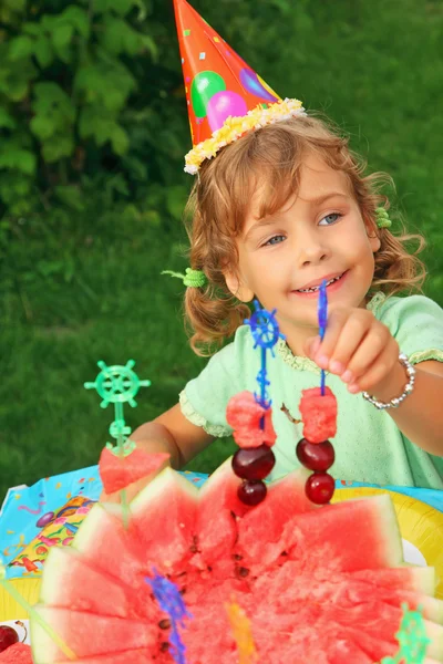 Malá holčička v čepici jí ovoce v zahradě, šťastné narozeniny — Stock fotografie