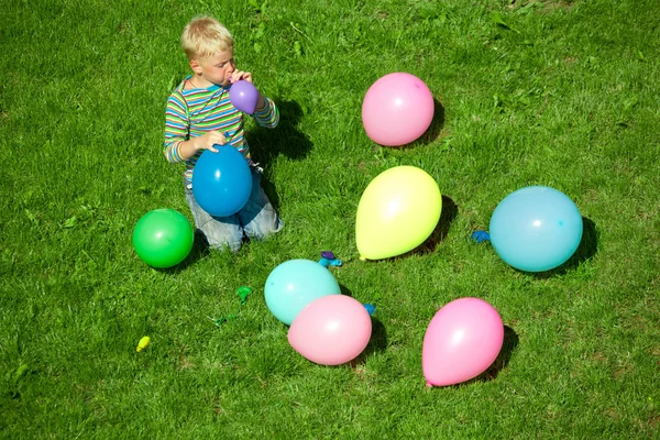 Pojken blåser upp ballonger, sitter på en gräs — Stockfoto