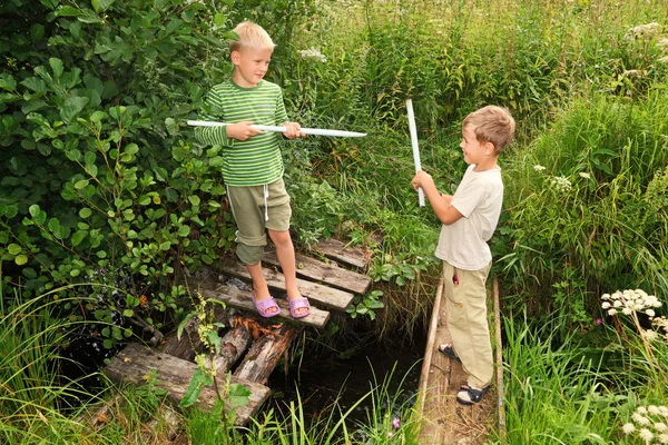 Two boys with sticks battling for fun on bridges over stream — Stock Photo, Image