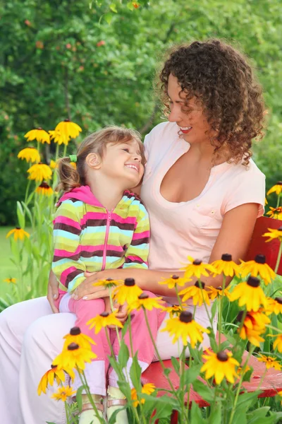 Молода жінка з маленькою дівчинкою сидить на лавці в саду — стокове фото