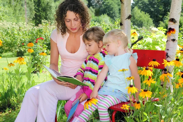Jonge vrouw leest het boek naar twee kleine meisjes in tuin — Stockfoto