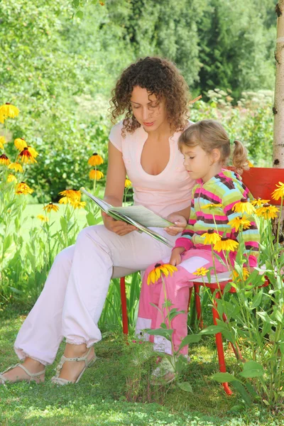 Ung kvinna läser boken till liten flicka i trädgården — Stockfoto