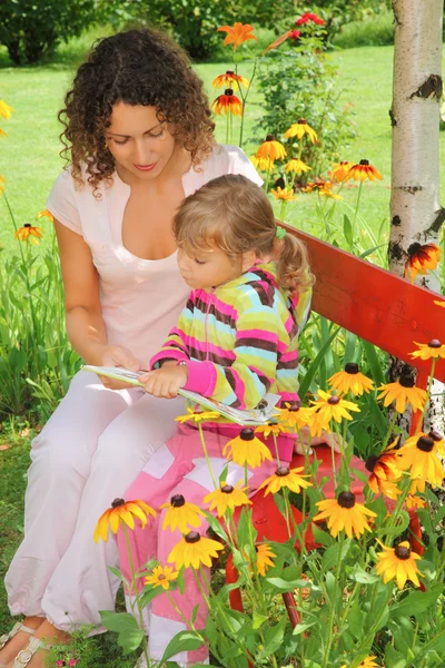 Νεαρή γυναίκα διαβάζει το βιβλίο για το μικρό κορίτσι στον κήπο — Φωτογραφία Αρχείου