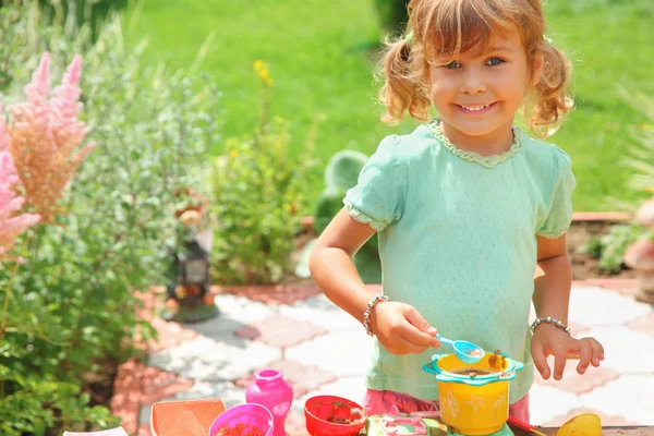 Smiling little girl plays cook in garden — Stock Photo, Image