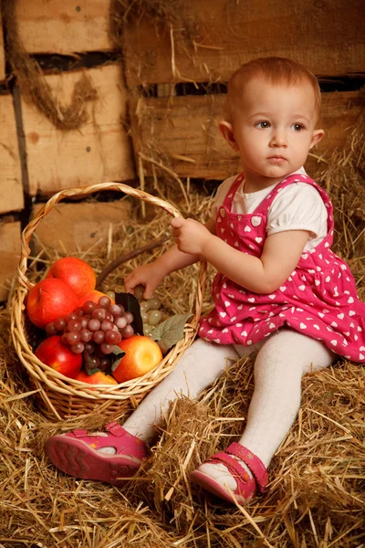 Das kleine Mädchen auf Stroh mit einem Korb — Stockfoto