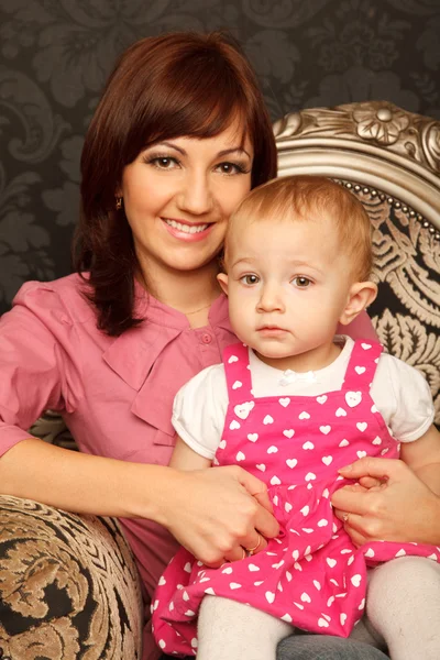 Mother and daughter on her lap sitting in armchair. Interior in — Stock Photo, Image