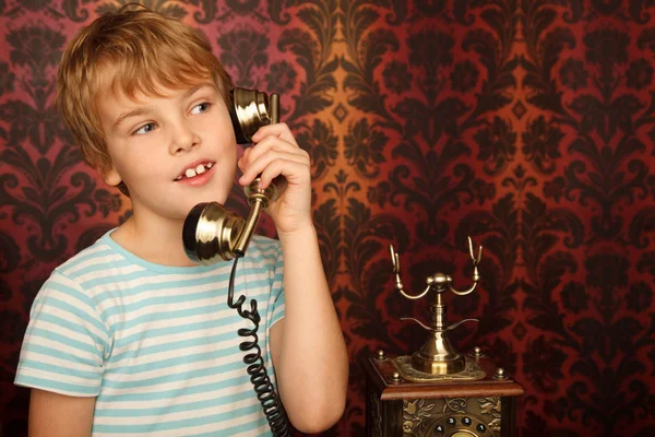 Portrait of boy in T-shirt talking to an old phone against wall — Stock Photo, Image
