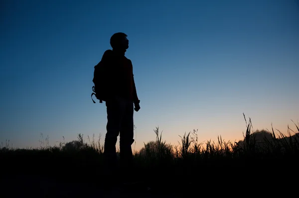 Silhuett av mannen med en ryggsäck mot den mörka himlen — Stockfoto
